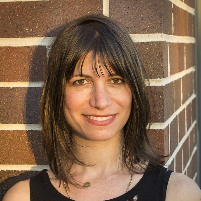 Joanna Fishman, Co-Director of Associated Counsellors & Psychologists Sydney, smiling in front of a brick wall
